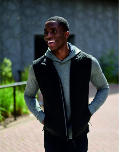 Bodywarmers Smiling man in a grey hoodie and black vest standing outdoors.