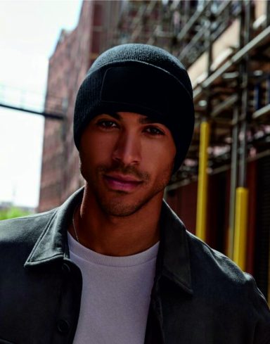 Headwear Young man wearing a black beanie and grey jacket, standing in an urban environment.